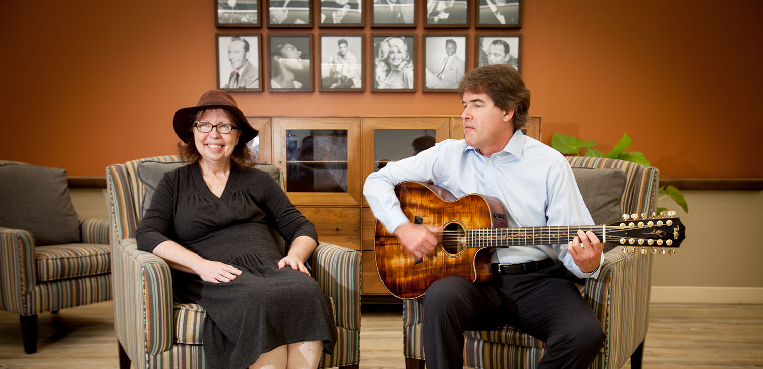 Woman sitting next to a man who is playing guitar