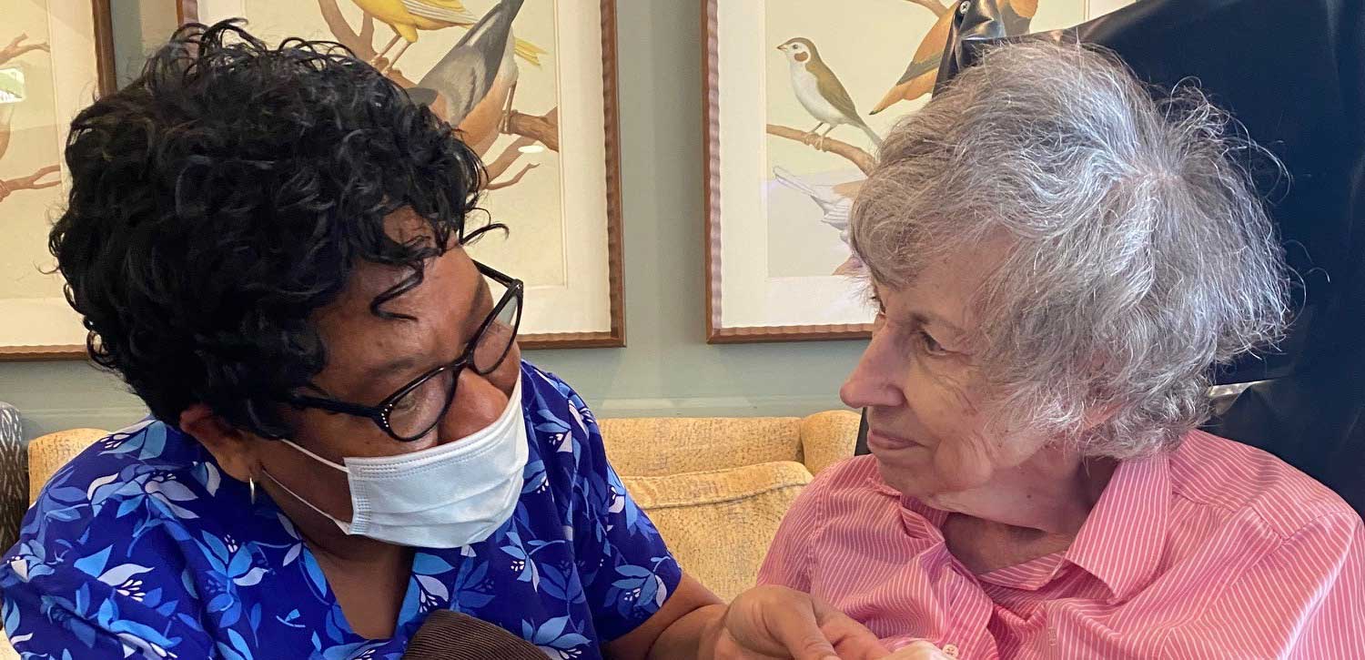 Caregiver wearing a mask speaking with a senior woman