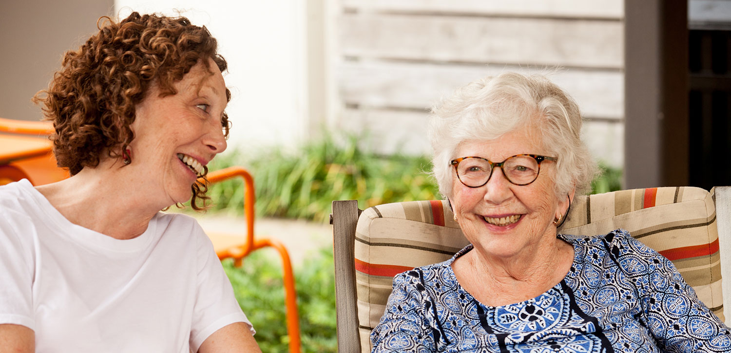 Senior woman and daughter sitting together on a couch and laughing