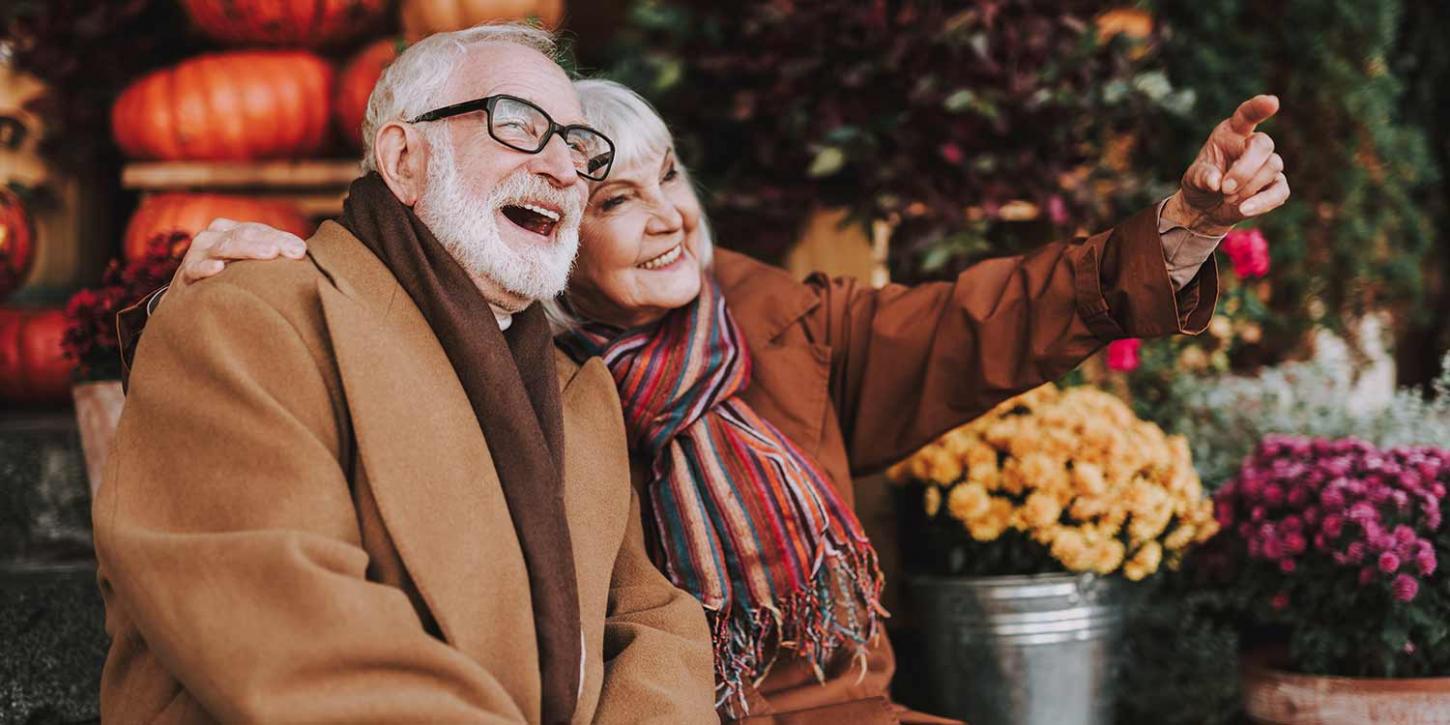 Senior couple bundled up outdoors with pumpkins in the background.