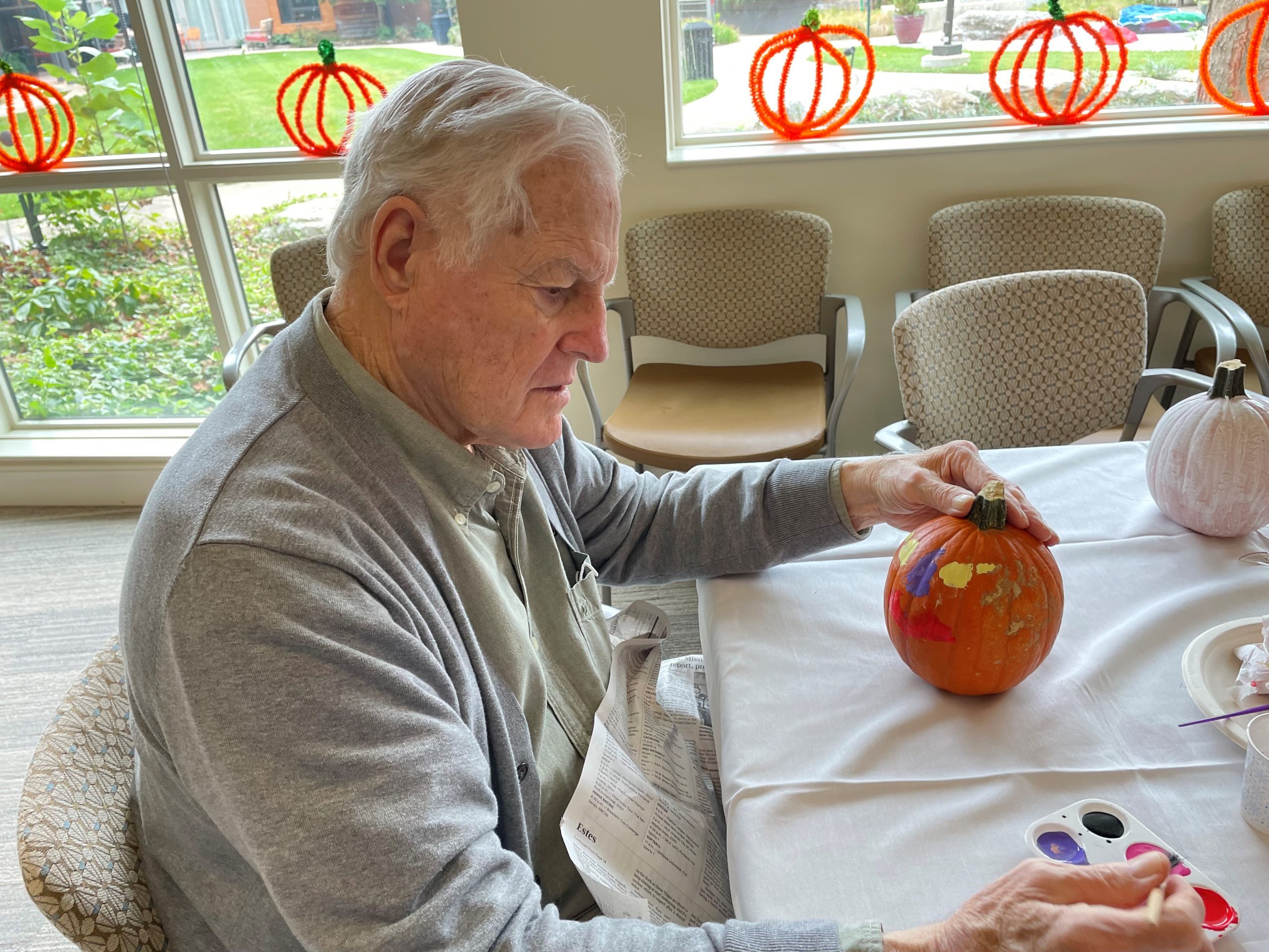 Senior man decorates a medium size pumpkin using acrylic paints