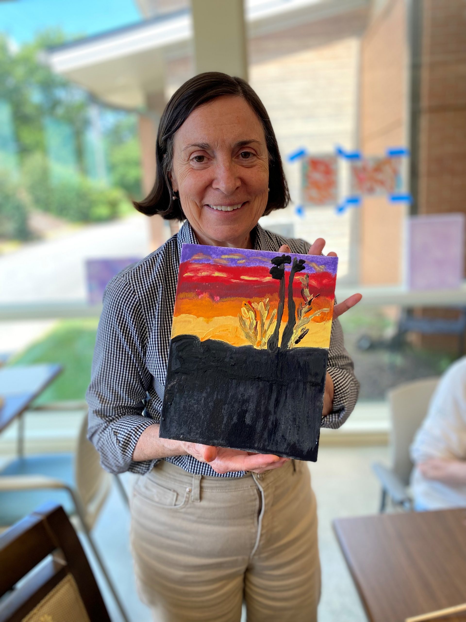 Abe's Garden Club member poses with colorful painting of sunset during art therapy