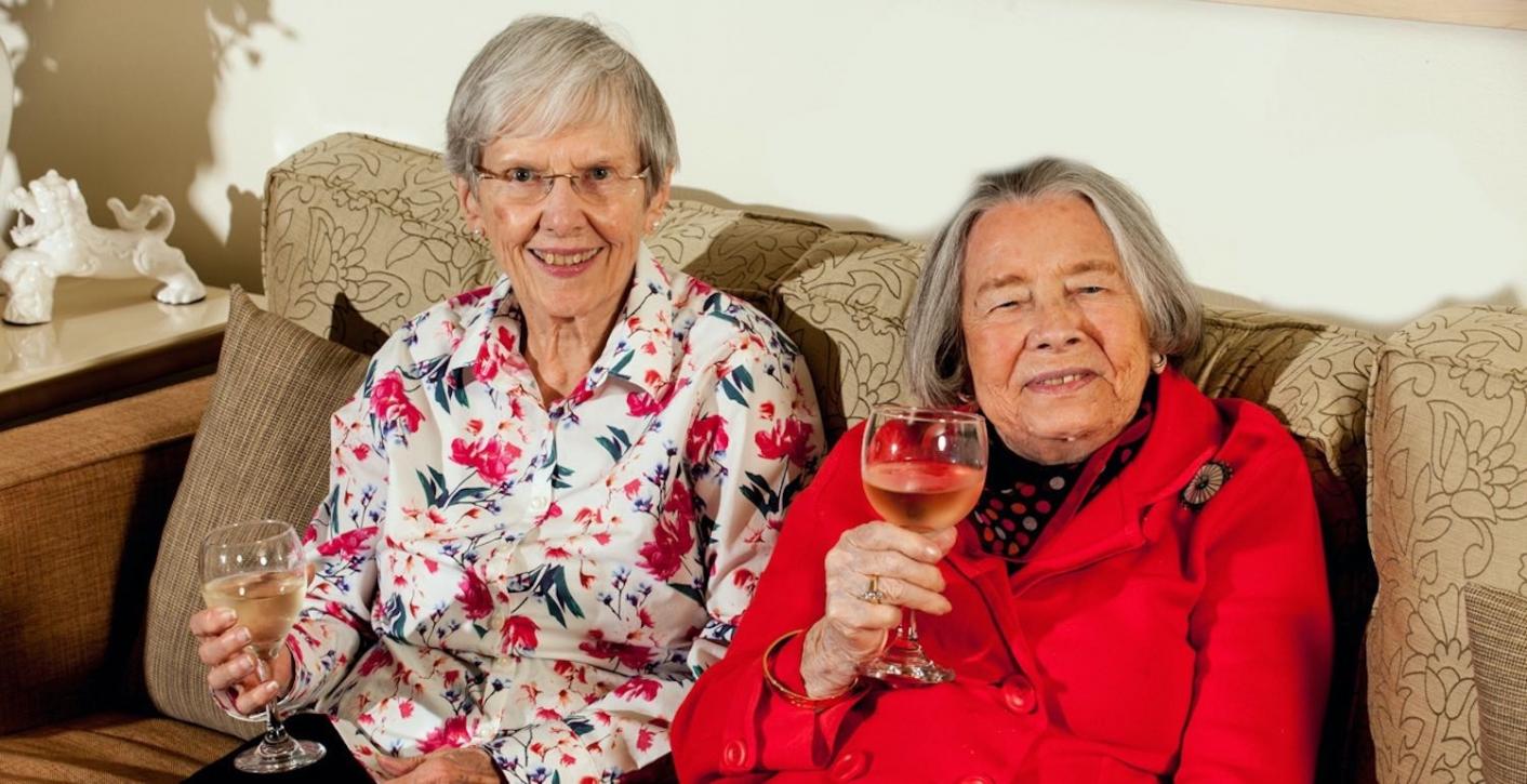 Two Abe's Garden Community residents sitting on couch with glasses of wine