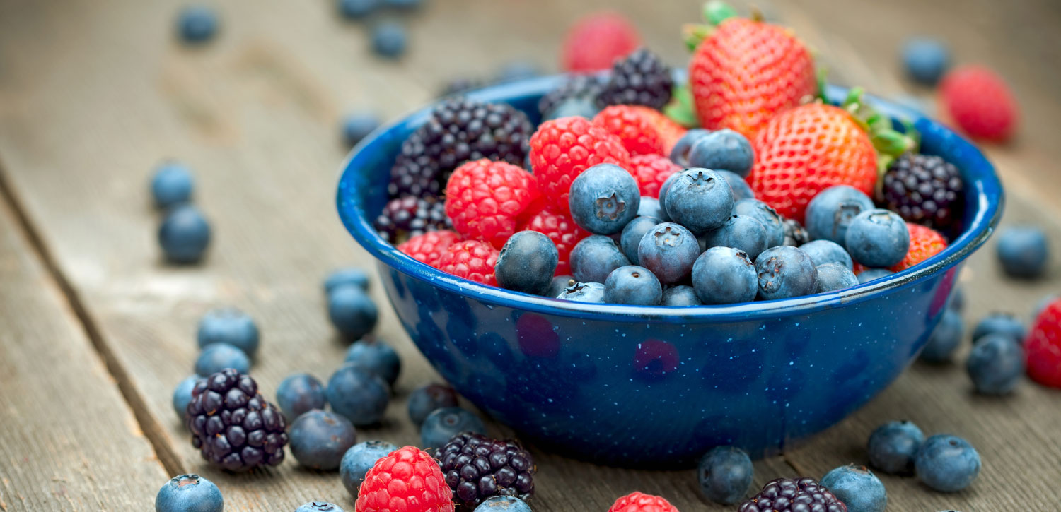 A blue bowl full of assorted berries on a wooden table