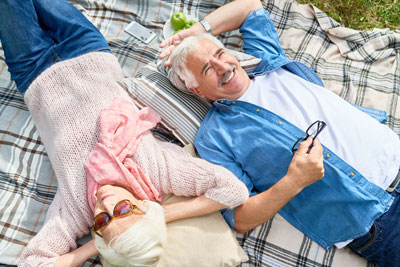 Senior aged husband and wife laying on picnic blanket outside