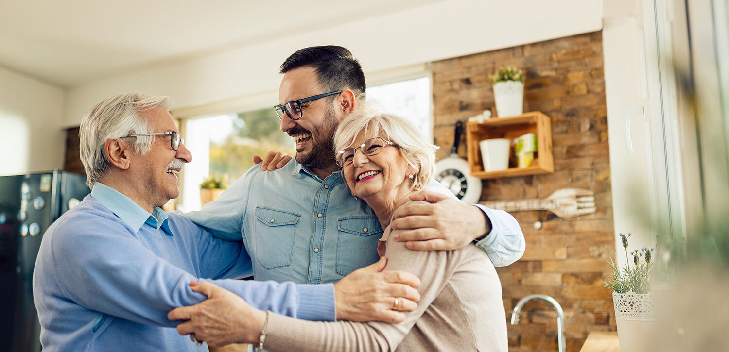 Male and female independent living residents hugging adult son in their new apartment