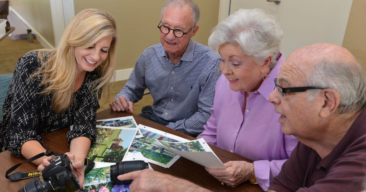 Group of seniors looking at photos with adult woman at an independent living community.